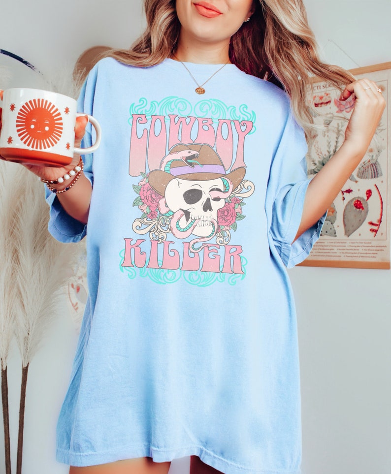 Op de afbeelding: Lichtblauw oversized T-shirt met een grafische print van een schedel met een cowboyhoed en een slang. De tekst "COWBOY KILLER" is gedrukt in een retro-lettertype.