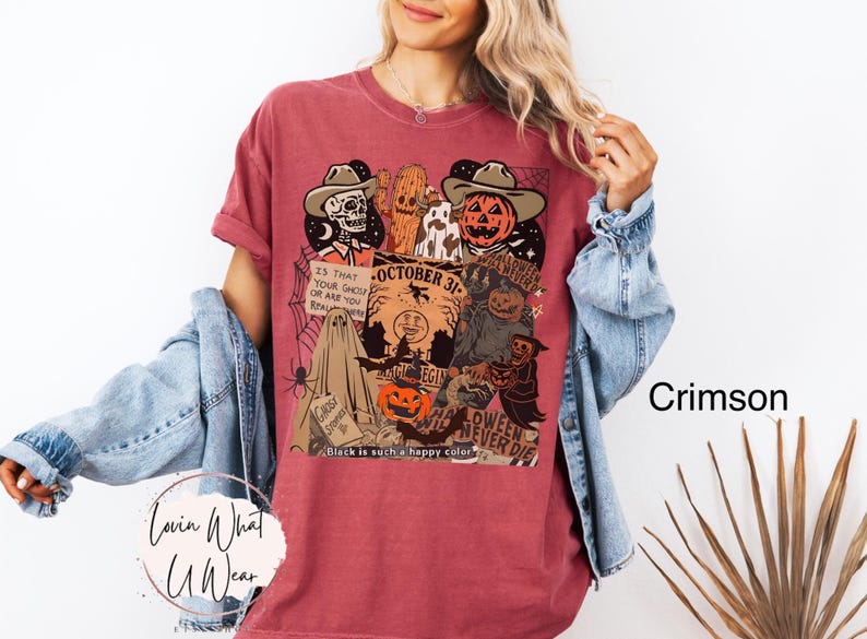 May include: Crimson-colored t-shirt with a Halloween-themed graphic. The design features a skull, a pumpkin, and other spooky characters. Text includes "October 31" and "Halloween Never Die". The shirt is a comfortable fit.