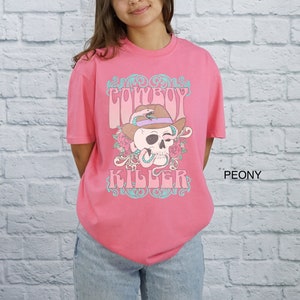 Op de afbeelding: Roze T-shirt met een afbeelding van een schedel met een cowboyhoed en een slang. De tekst "COWBOY KILLER" is onder de schedel gedrukt.