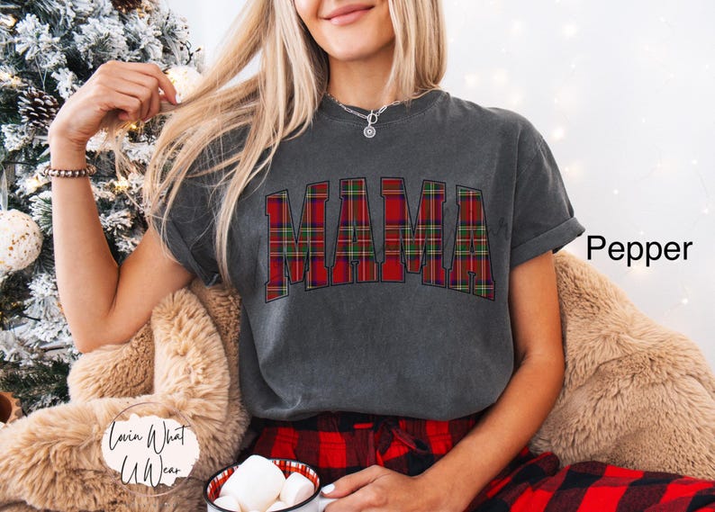 May include: A dark gray t-shirt with the word "MAMA" in a red and green plaid pattern. The shirt is part of a casual outfit, paired with red plaid pajama pants. The word "Pepper" is written in black on the right side of the image.