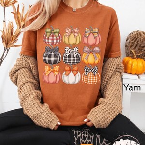 Peut inclure: T-shirt orange avec un motif de neuf citrouilles orn&eacute;es de n&oelig;uds vari&eacute;s. Les citrouilles sont de couleurs diff&eacute;rentes, comme l'orange, le rose et le blanc. Les n&oelig;uds pr&eacute;sentent des motifs &agrave; carreaux et &agrave; pois. Le t-shirt fait partie d'une collection sur le th&egrave;me de l'automne.