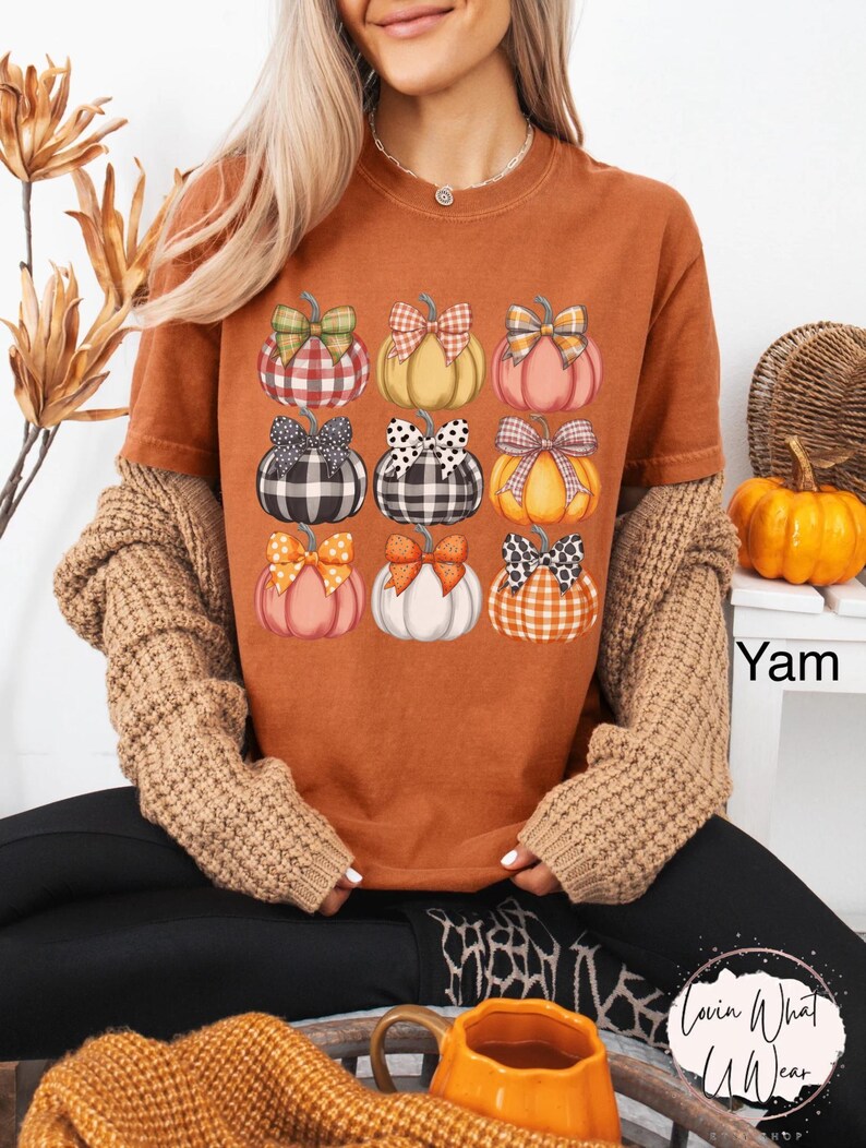 Peut inclure: T-shirt orange avec un motif de neuf citrouilles orn&eacute;es de n&oelig;uds vari&eacute;s. Les citrouilles sont de couleurs diff&eacute;rentes, comme l'orange, le rose et le blanc. Les n&oelig;uds pr&eacute;sentent des motifs &agrave; carreaux et &agrave; pois. Le t-shirt fait partie d'une collection sur le th&egrave;me de l'automne.