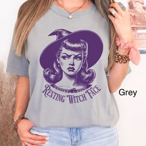 May include: A grey t-shirt with a purple graphic of a woman with a witch hat and the text "Resting Witch Face".