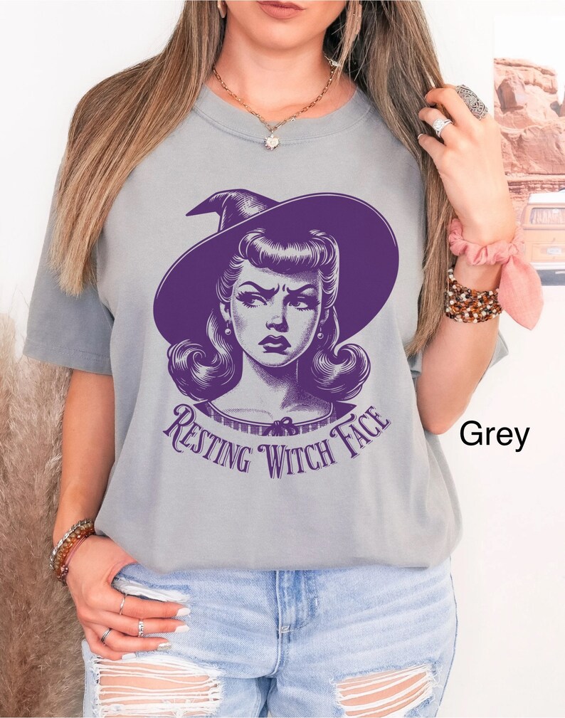 May include: A grey t-shirt with a purple graphic of a woman with a witch hat and the text "Resting Witch Face".