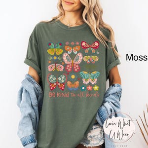 May include: A moss green t-shirt with a colorful butterfly design and the text "Be Kind to all kinds".