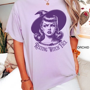 May include: A purple t-shirt with a graphic of a woman with a witch hat and the text "Resting Witch Face".