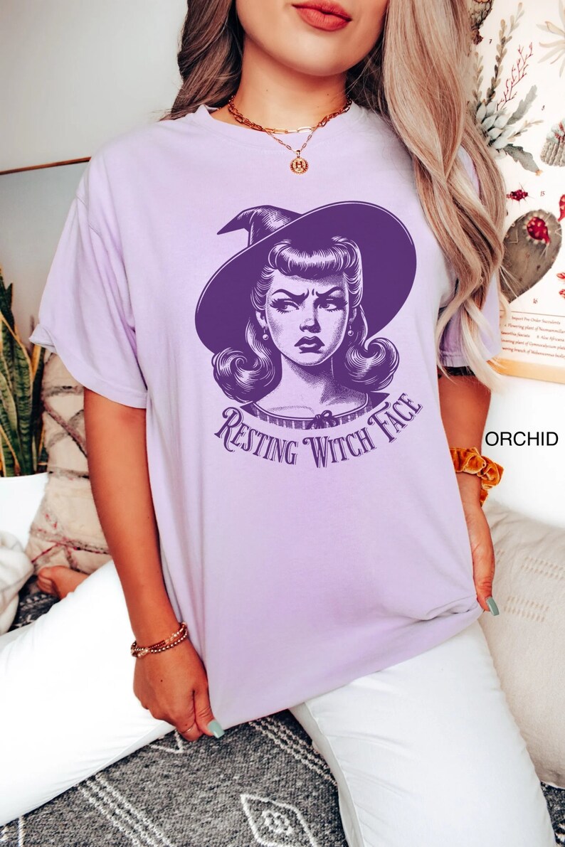 May include: A purple t-shirt with a graphic of a woman with a witch hat and the text "Resting Witch Face".