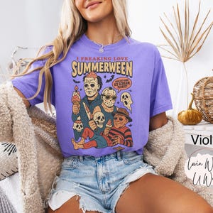 K&ouml;nnte beinhalten: Violettes T-Shirt mit dem Text "I Freaking Love Summerween" und einer Grafik von Horrorfilmfiguren mit Eiscreme. Das Design beinhaltet Totenk&ouml;pfe und Flederm&auml;use. Teil einer Bekleidungskollektion.