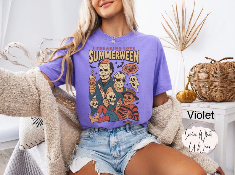 K&ouml;nnte beinhalten: Violettes T-Shirt mit dem Text "I Freaking Love Summerween" und einer Grafik von Horrorfilmfiguren mit Eiscreme. Das Design beinhaltet Totenk&ouml;pfe und Flederm&auml;use. Teil einer Bekleidungskollektion.