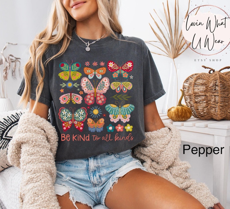 May include: A dark gray t-shirt with a colorful butterfly design and the text "Be Kind to all kinds".