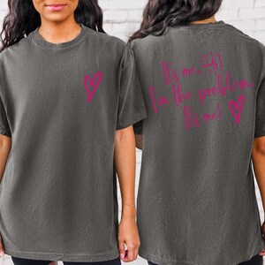 May include: A dark gray t-shirt with a pink heart on the front and the text "It's me, I'm the problem. It's me!" on the back.