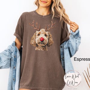 K&ouml;nnte beinhalten: Ein braunes T-Shirt mit einem Aufdruck eines Hundes, der ein Rentiergeweih-Stirnband und eine rote Nase tr&auml;gt. Der Text "Espresso" ist im Hintergrund sichtbar.