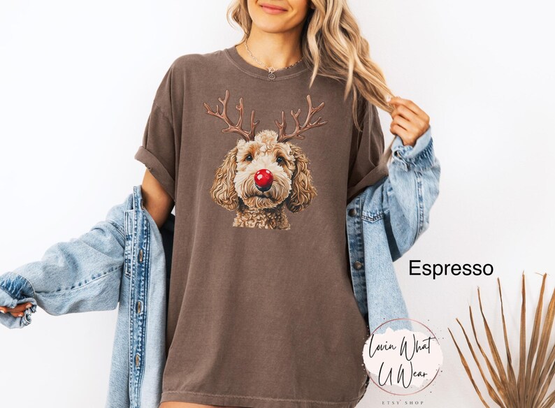 K&ouml;nnte beinhalten: Ein braunes T-Shirt mit einem Aufdruck eines Hundes, der ein Rentiergeweih-Stirnband und eine rote Nase tr&auml;gt. Der Text "Espresso" ist im Hintergrund sichtbar.