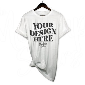 May include: White t-shirt with the text "YOUR DESIGN HERE" in black, with the words "Mockup Sisters" in smaller font below.