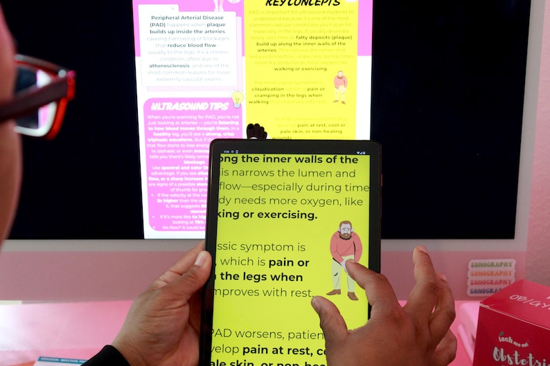 May include: A person holding a tablet displaying medical information about Peripheral Arterial Disease (PAD). The tablet screen shows text and an illustration of a person. A computer monitor and a box are in the background.