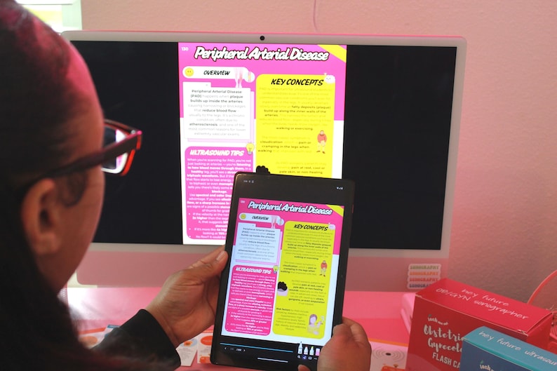 May include: A person wearing glasses is looking at a computer monitor and a tablet displaying information about Peripheral Arterial Disease. The monitor and tablet show text and graphics in pink, yellow, and white.