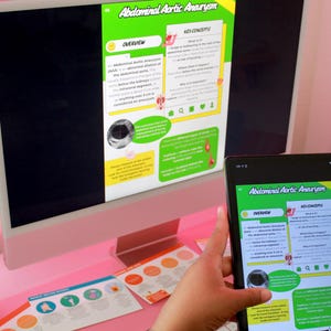 May include: A desktop computer and tablet displaying educational content about Abdominal Aortic Aneurysm. The computer screen and tablet show the same information, with a green and yellow color scheme. Other educational materials are on the desk.
