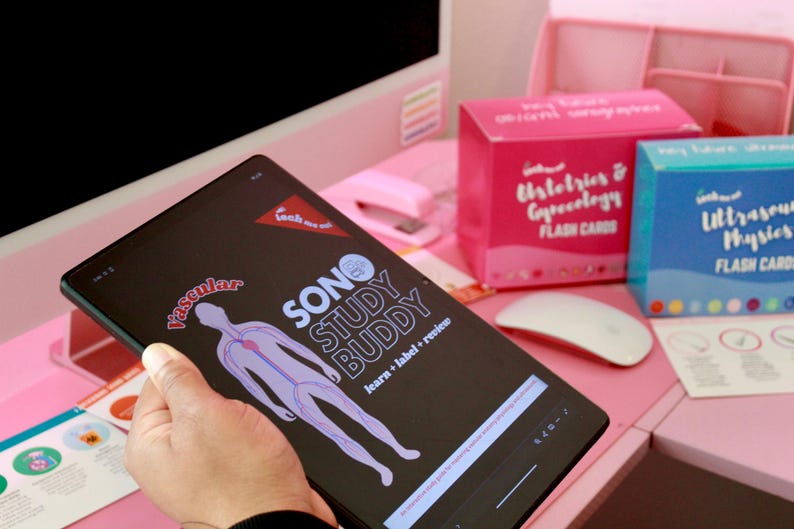 May include: A tablet displaying the "SONO STUDY BUDDY" app with a vascular diagram. Pink and blue flashcard boxes for "Histology & Gynecology" and "Ultrasound Physics" are visible, along with a white mouse, on a pink desk.