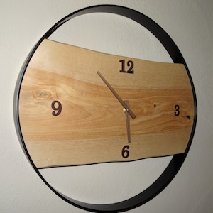 Könnte beinhalten: Eine Holzuhr mit einem schwarzen Metallrahmen. Das Zifferblatt der Uhr hat römische Ziffern und eine Holzmaserung. Die Zeiger der Uhr sind aus Holz.