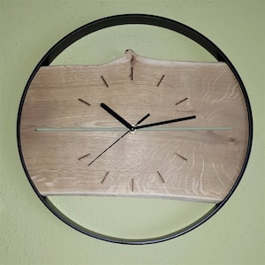 Könnte beinhalten: Eine runde Uhr mit schwarzem Rahmen und einem Holzgesicht. Die Uhr hat schwarze Zeiger und ein hellbraunes Holzmaserungsmuster.