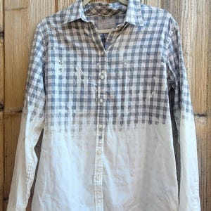 May include: A white and gray gingham button-down shirt with a faded ombre effect. The shirt has a relaxed fit and long sleeves.