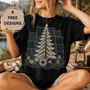Puede incluir: Una camiseta negra de manga corta con un gráfico de un pino, montañas y una brújula. El diseño incluye un fondo de patchwork de cuadrados verde oscuro y azul con detalles de costura blancos y acentos florales en la base.