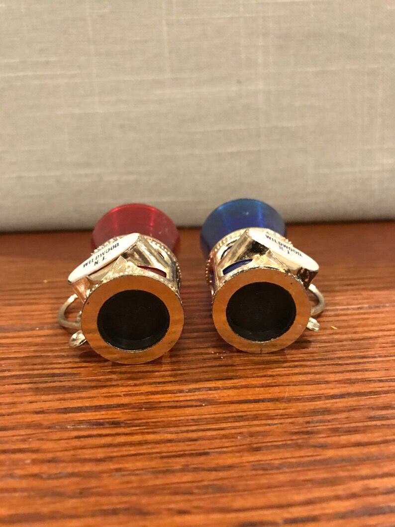 May include: Two miniature souvenir shot glasses with gold rims. The glasses are red and blue with white accents. The glasses have the words "Wildwood N.J." printed on them.