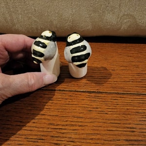 May include: Two ceramic bee salt and pepper shakers. The bee designs are black and white with yellow accents. The shakers are white.