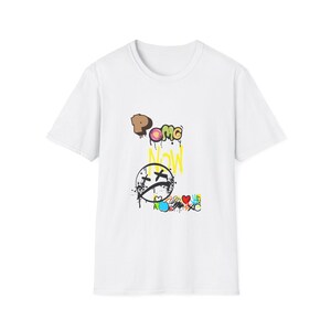 Può includere: T-shirt bianca con un design grafico colorato. Il design include le parole "OMG Now" in lettering in stile graffiti, una faccia triste con gli occhi a X e vari altri scarabocchi colorati. La maglietta è realizzata in un materiale morbido.