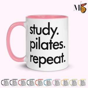 May include: White ceramic mug with a pink interior and handle. The mug features the words "study. pilates. repeat." in large black letters. A butterfly logo is in the upper right corner. Several smaller mugs with different color accents are shown below.