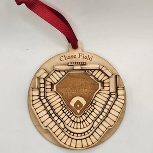 May include: A wooden ornament in the shape of Chase Field, with a red ribbon for hanging. The stadium design is laser-cut, showing the seating and field details. The text "Chase Field" is above the stadium.