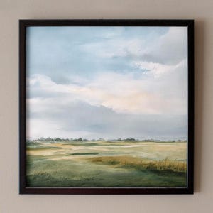 May include: Framed landscape art showing a field beneath a cloudy sky. The painting uses greens, yellows, and blues, with a dark brown frame. The artwork creates a sense of peace and natural beauty, suitable for home decor.