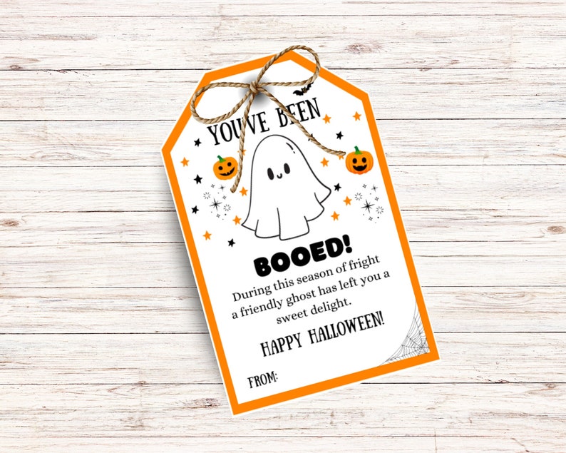 May include: A Halloween-themed gift tag with an orange border and a string bow. The tag features a friendly ghost illustration, pumpkins, stars, and the text "YOU'VE BEEN BOOED!" and "HAPPY HALLOWEEN!" on a white background.