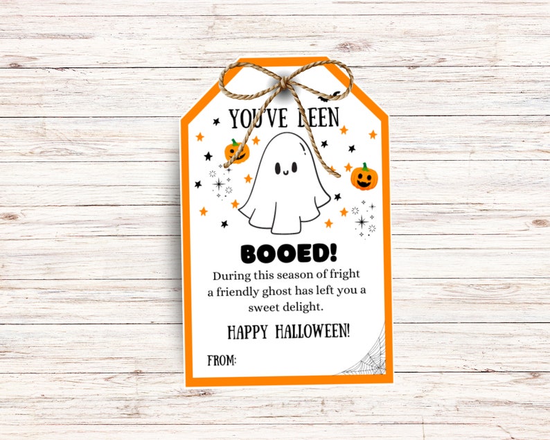 May include: A Halloween-themed gift tag with an orange border and a jute twine bow. The tag features a cartoon ghost, pumpkins, stars, and the text "YOU'VE BEEN BOOED!" and "HAPPY HALLOWEEN!" on a white background.