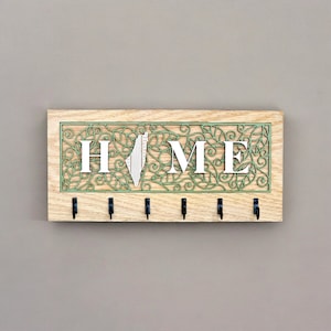 May include: A wooden key holder with a green leafy design and the word "HOME" in white letters. The key holder has six hooks for hanging keys.