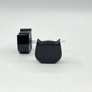 May include: Two black cat-shaped ear plugs. The ear plugs are made of a smooth, glossy material.