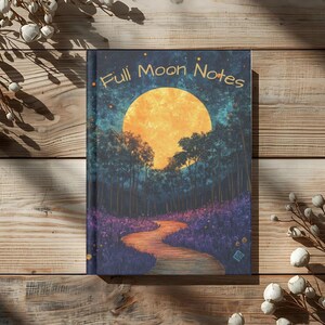 May include: A hardcover notebook with the title "Full Moon Notes" features a vibrant illustration of a large orange moon over a forest with a winding path. The cover art is set against a dark blue and purple sky and forest, with a wooden background.