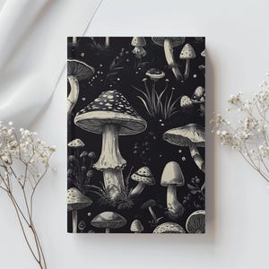 May include: A black and white notebook featuring a repeating pattern of various mushrooms. The mushrooms have detailed caps and stems, with some having speckled patterns. The background is a solid black, creating a high-contrast design.