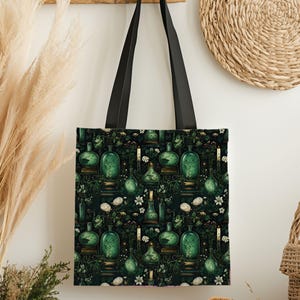 May include: A black tote bag with black handles. The bag features a repeating pattern of green glass bottles, candles, and white flowers on a dark green background. The design has a vintage, apothecary theme.