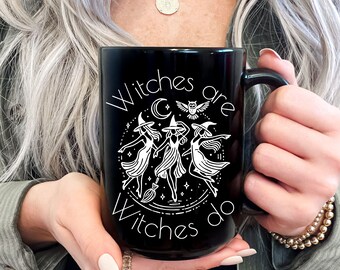 May include: Black ceramic mug with the words "Witches are Witches do" in white script. The mug features a white graphic of three witches dancing around a broom, with a crescent moon and an owl.