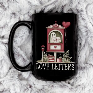 May include: Black ceramic mug featuring a whimsical design of a red and white mailbox with a ghost holding a letter that says "Love". A red heart balloon floats above the mailbox, and the words "LOVE LETTERS" are printed below.