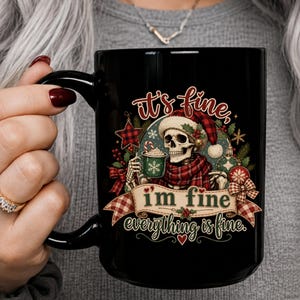 May include: A black ceramic mug featuring a graphic of a skeleton wearing a Santa hat and plaid scarf, holding a green mug with a candy cane. The text reads, it's fine, i'm fine, everything is fine, surrounded by festive holiday decorations.