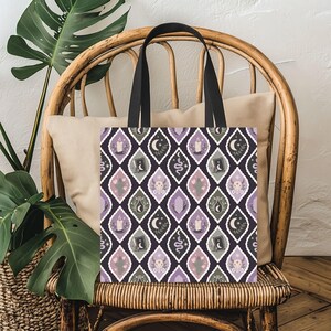 May include: A black tote bag featuring a repeating pattern of diamond-shaped frames. Inside each frame are illustrations of candles, crescent moons, snakes, skulls, cacti, crystals, and potion bottles in shades of purple, green, and white.