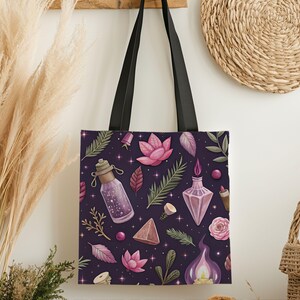 May include: A purple tote bag with black handles, featuring a repeating pattern of pink lotus flowers, potion bottles, leaves, and crystals. The design includes a starry background and botanical elements.