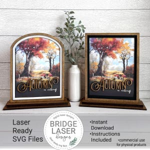 May include: Two wooden framed art pieces with an autumn landscape scene. The artwork features a colorful tree with red, orange, and yellow leaves. The words "Autumn is calling" are displayed on the bottom of the artwork. A white vase with a green plant is between the two framed art pieces.