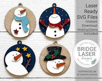 May include: Four laser-cut wooden snowman ornaments with different designs. The ornaments are round and feature a white snowman with black eyes and a red nose. One snowman has a blue scarf, another has a red scarf, another has a black top hat with holly, and the last one has a blue background with stars. The text "Laser Ready SVG Files" is visible in the image.