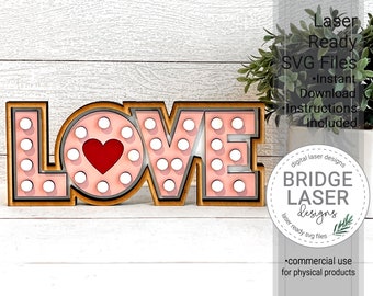 May include: A pink and brown wooden sign with the word "LOVE" in large letters. The letters are decorated with white polka dots and a red heart in the center of the "O". The sign is laser cut and ready to be assembled.