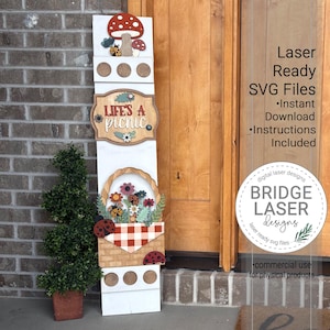 May include: A white wooden sign with a mushroom and ladybug design at the top, the words "LIFE'S A PICNIC", and a basket of flowers and ladybugs. The sign is decorated with laser-cut details and is designed for outdoor use.