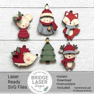 May include: A collection of wooden Christmas ornaments in various shapes, including a mouse, penguin, fox, hedgehog, Christmas tree, and reindeer. Each ornament is painted with festive colors and details. The image also includes text that says "Laser Ready SVG Files" and "BRIDGE LASER designs".