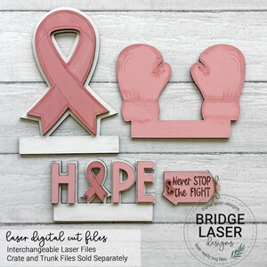 May include: A set of laser-cut wooden shapes including a pink awareness ribbon, two pink boxing gloves, the word HOPE with a ribbon replacing the letter O, and a small sign with the text Never STOP the FIGHT and a small ribbon icon.